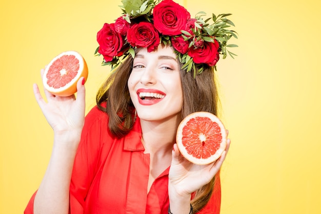 Retrato colorido de uma linda mulher com uma guirlanda de flores segurando fatias de toranjas no fundo amarelo