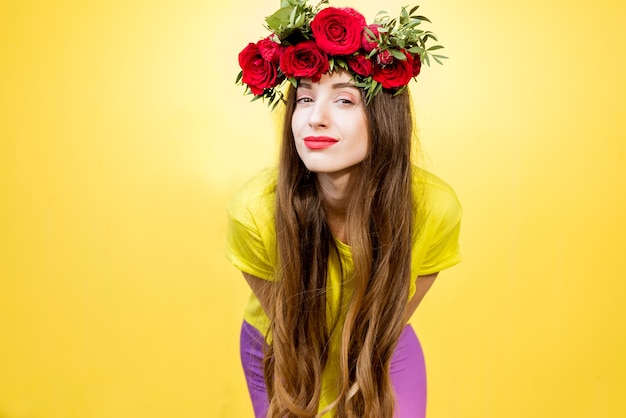 Retrato colorido de uma linda mulher em uma camiseta amarela com coroa de rosas vermelhas sobre fundo amarelo