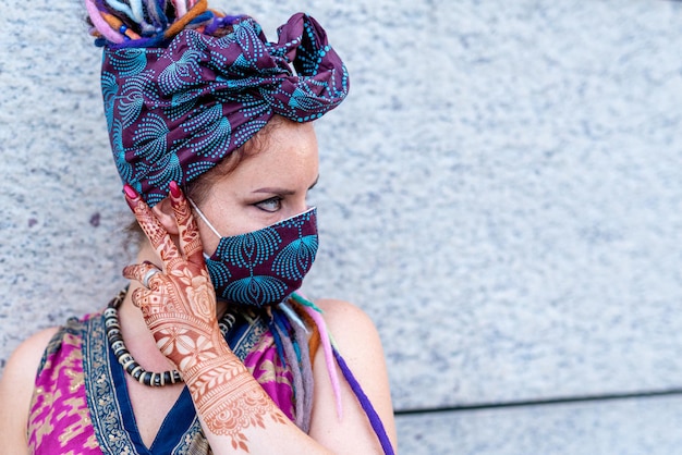 Retrato colorido mujer con ojos azules humor misterioso y pose máscara protectora hecha a mano para coronavirus utilizada en estilo de moda gitana que está mirando hacia un nuevo futuro sin pandemia de coronavirus