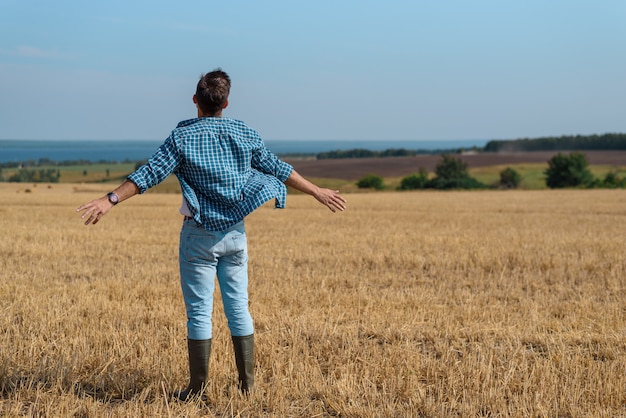 Retrato com costas de um homem de jeans, camisa, botas de borracha no campo com as mãos abertas