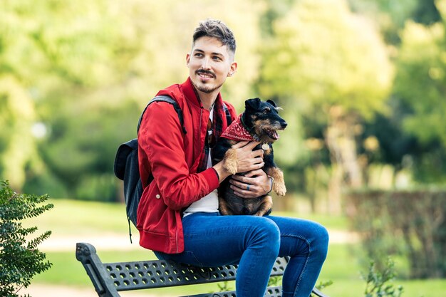 Retrato com foco seletivo em um homem distraído segurando um cachorro enquanto está sentado em um banco de um parque