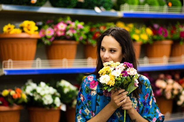 Retrato com foco seletivo em uma mulher sorridente segurando um balde de flores em uma floricultura