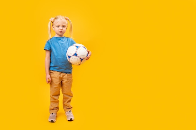 Retrato completo de criança de 56 anos com bola de futebol isolada em fundo amarelo Menina caucasiana com cabelo loiro adora futebol