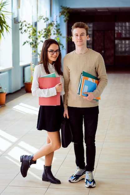 Retrato completo de estudantes sorridentes com livros e pastas no corredor da universidade