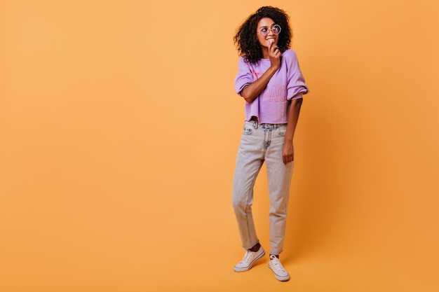 Retrato completo de uma garota magra fascinante com penteado ondulado foto interna de uma mulher bonita pensativa isolada em fundo amarelo