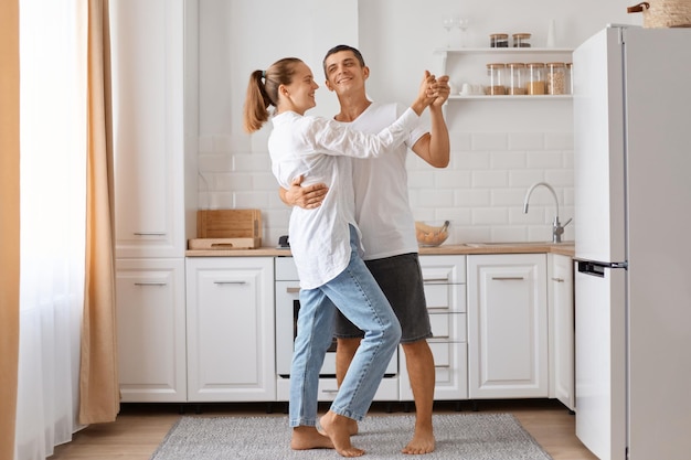 Retrato completo de hombre y mujer adulta joven atractiva bailando cocina pareja romántica pasar tiempo juntos en casa expresando amor y gentil