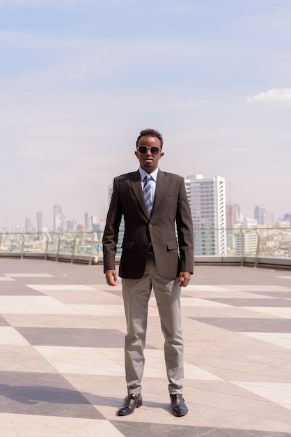 Retrato completo de un hombre de negocios africano con traje y corbata al aire libre en la ciudad mientras está de pie