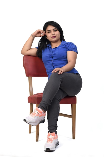 Retrato completo de una mujer latinoamericana sentada y mirando a cámara y seria sobre fondo blanco.