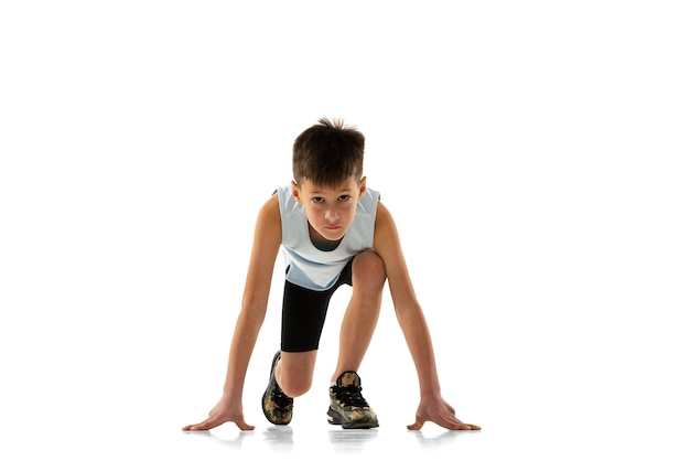 Retrato completo de niño atleta de pie en posición para correr aislado sobre fondo blanco.