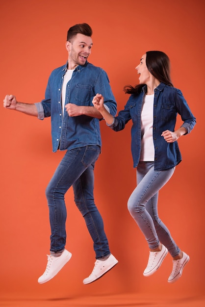 Retrato completo de una pareja joven alegre y emocionada saltando juntos y celebrando el éxito mientras corren aislados en el estudio