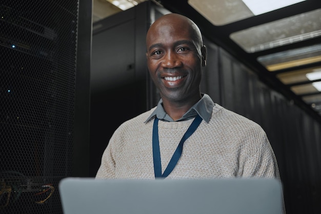Retrato de computadora portátil y hombre negro de TI en la sala de servidores para el ingeniero de investigación que trabaja en el vestíbulo del centro de datos oscuro.