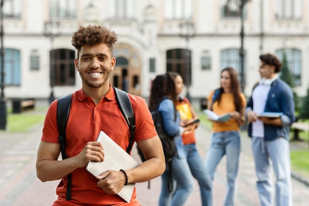 Retrato conceitual de ensino superior de um estudante negro feliz posando ao ar livre