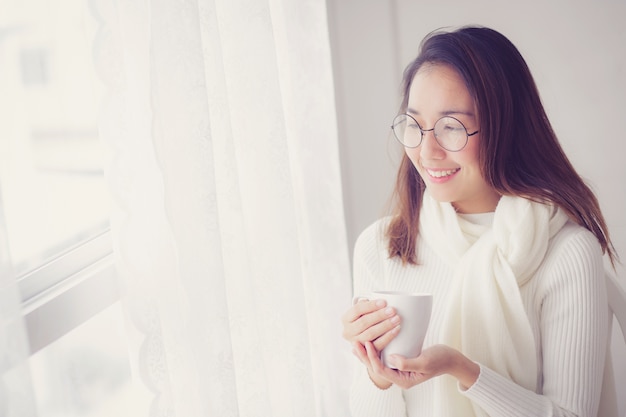 Retrato del concepto del dormitorio: mujer asiática que sostiene una taza de café con el dormitorio