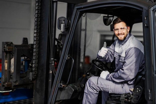 Retrato de un conductor de montacargas feliz en la fábrica dando su visto bueno para la entrega a tiempo