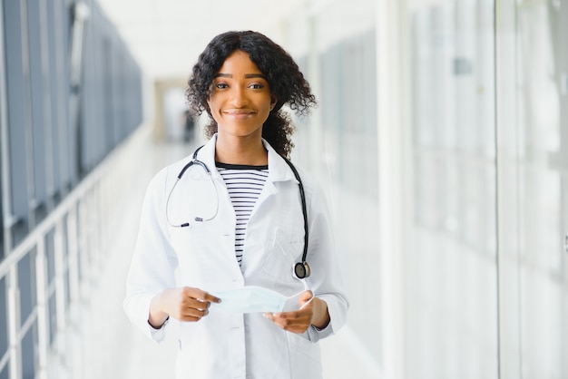Retrato confía en afroamericana doctora profesional médica escribiendo notas de pacientes aisladas sobre fondo de ventanas de pasillo de clínica de hospital. Expresión facial positiva