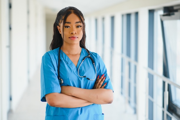 Retrato confía en afroamericana doctora profesional médico escribiendo notas de pacientes aisladas sobre fondo de ventanas de pasillo de clínica de hospital. Expresión facial positiva