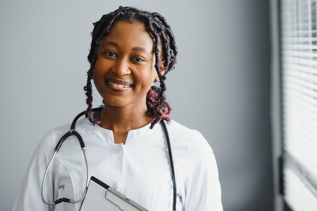 Retrato confiado doctora africana profesional médico escribiendo notas de pacientes aisladas en el fondo de las ventanas del pasillo de la clínica del hospital Expresión facial positiva