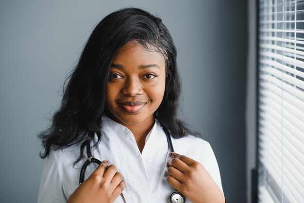 Retrato confiado doctora africana profesional médico escribiendo notas de pacientes aisladas en el fondo de las ventanas del pasillo de la clínica del hospital Expresión facial positiva