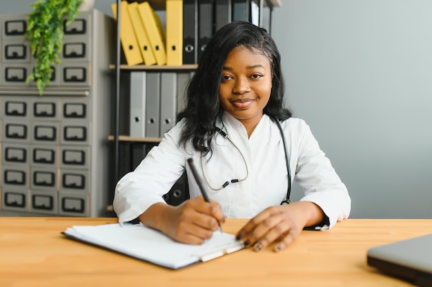 Foto retrato confiante médico feminino africano profissional médico escrevendo notas do paciente isoladas no fundo das janelas do corredor da clínica do hospital expressão facial positiva