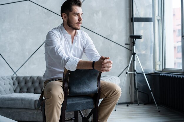 Retrato de confianza. Longitud total de hombre joven pensativo en traje completo mirando a otro lado mientras está sentado en el taburete.