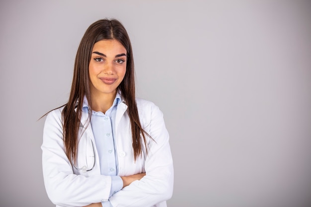 Foto retrato de confianza sonriente doctora. el profesional médico adulto medio lleva una bata de laboratorio y un estetoscopio. ella está de pie contra la pared gris en el hospital.