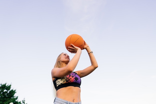 Retrato de confianza sonriente jugador de baloncesto femenino con balón en mano y mirando a la cámara