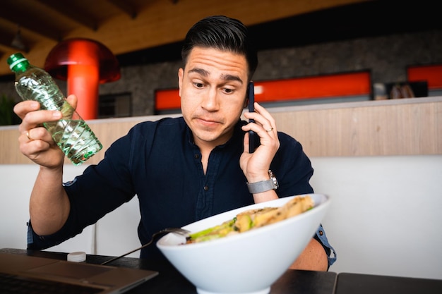 Retrato confundido hombre incierto hablando por teléfono sentado en la mesa almorzar saludable con ensalada