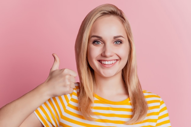 Retrato de consejero positivo chica rubia levantar el pulgar hacia arriba aprobar sobre fondo de color rosa