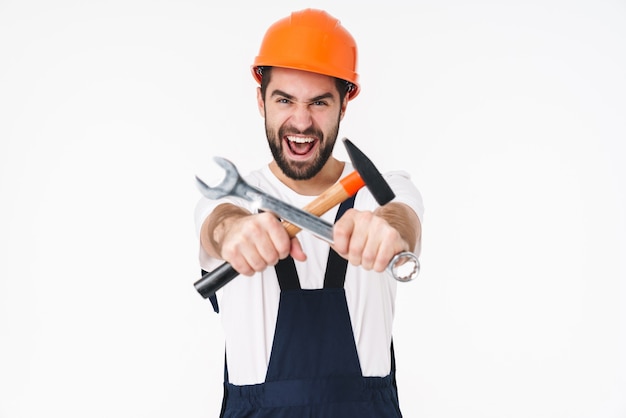 Retrato del constructor del hombre joven que grita en el casco que presenta aislado sobre la pared blanca que sostiene el equipo.