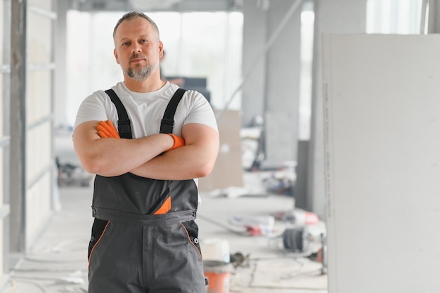 Retrato de un constructor en uniforme de trabajo con casco protector de pie con instrumentos en el sitio de construcción en el interior