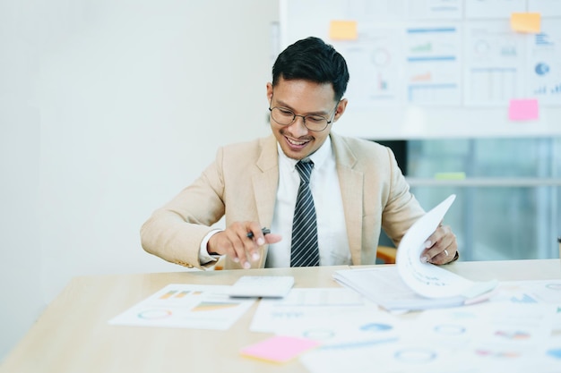 Retrato de un contador asiático que trabaja en un escritorio calculando impuestos de documentos financieros anuales usando una calculadora en el trabajo