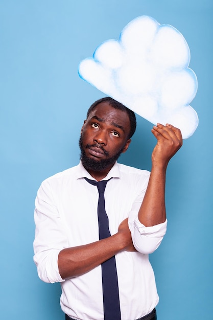 Retrato de un contador con camisa blanca mirando hacia la nube de ideas de papel blanco haciendo una lluvia de ideas frente a un fondo azul. Empresario afroamericano pensando bajo una burbuja de pensamiento.