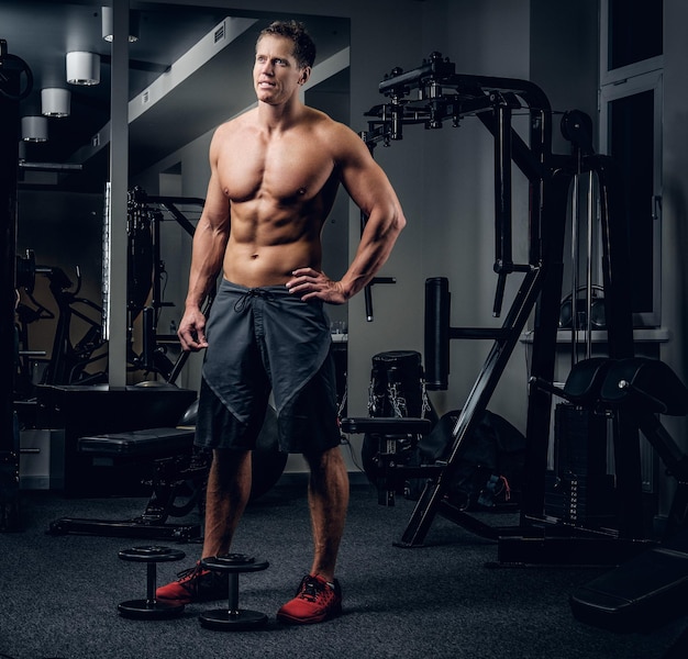 Retrato corporal completo de un hombre musculoso sin camisa en un club de gimnasia.