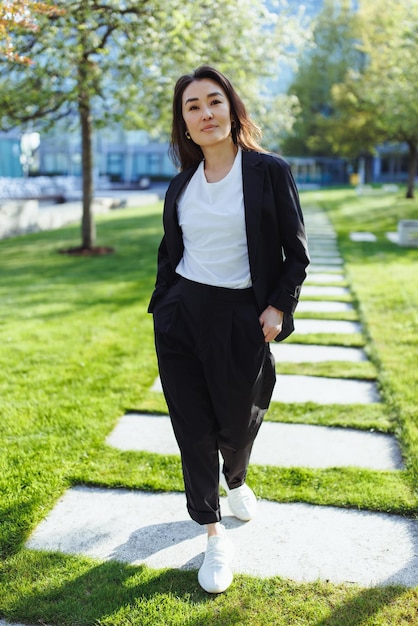 Retrato corporal completo de una mujer de negocios asiática confiada en traje caminando en el parque de primavera del centro de negocios