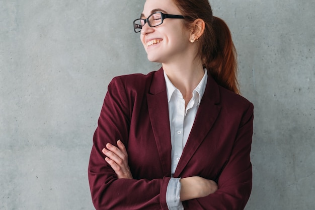 Retrato corporativo interno. Início da carreira. Mulher jovem sorridente com os braços cruzados.