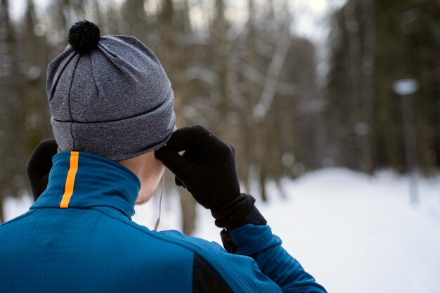 Retrato de un corredor de atrás usando audífonos y preparándose para correr en el bosque de invierno