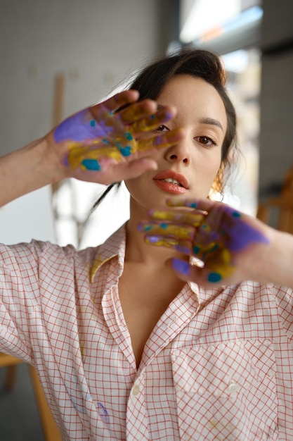 Retrato creativo de un joven artista mirando a la cámara a través de manos pintadas