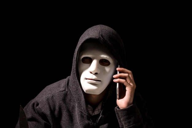 Retrato de un criminal con máscara usando un teléfono móvil contra un fondo negro