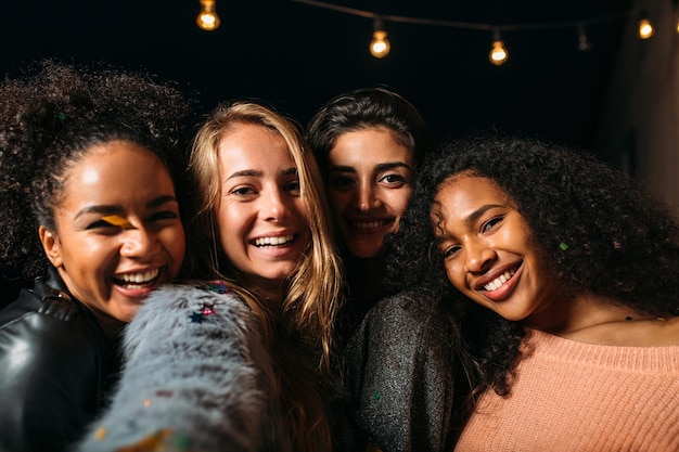 Retrato de cuatro mujeres diversas tomando selfies y sonriendo