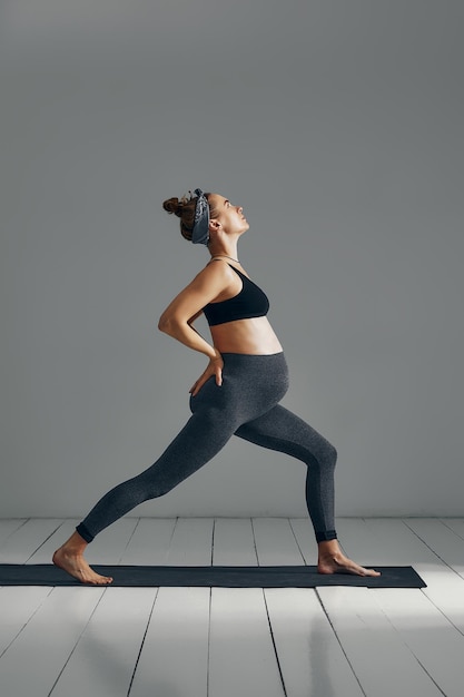 Retrato de cuerpo completo de mujer embarazada haciendo yoga en colchoneta aislado sobre fondo gris