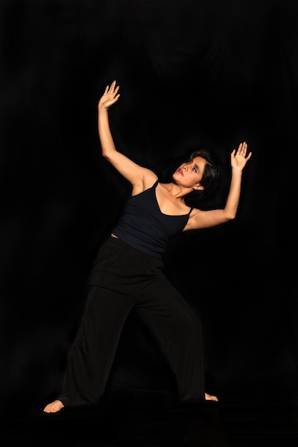 Retrato de cuerpo completo de una mujer latina posando aislada sobre fondo negro mirando y levantando los brazos Concepto de expresión corporal femenina
