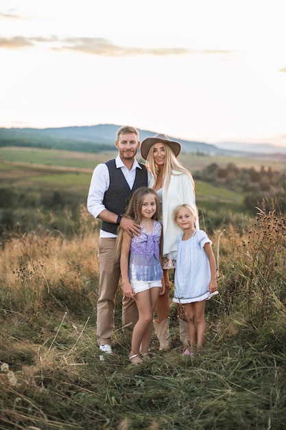 Retrato de cuerpo entero de la alegre familia caucásica, madre, padre y dos hijas pequeñas, de pie en el campo salvaje de verano