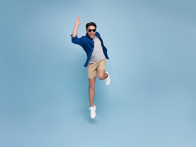 Retrato de cuerpo entero de un apuesto hombre asiático sonriente saltando aislado en el fondo azul del estudio