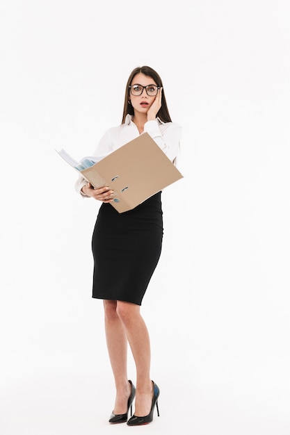 Retrato de cuerpo entero de una atractiva joven empresaria en ropa formal que se encuentran aisladas sobre la pared blanca, sosteniendo la carpeta