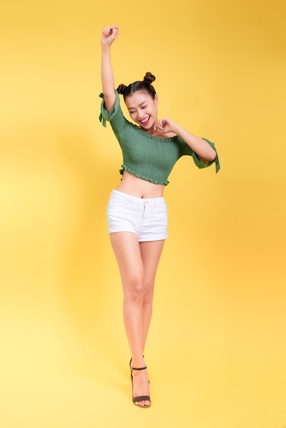 Retrato de cuerpo entero de una bella mujer joven con gafas de sol sobre fondo amarillo.