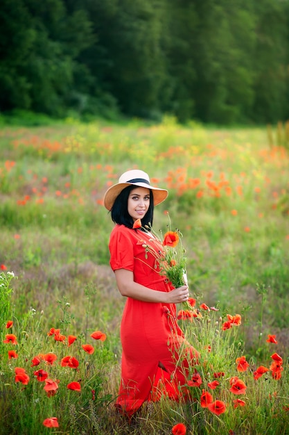 Retrato de cuerpo entero de una bella mujer joven con un vestido rojo en un campo de amapolas.