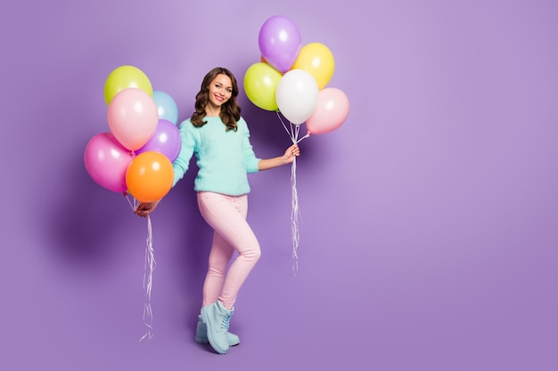 El retrato de cuerpo entero de una dama bastante divertida trae muchos globos de aire coloridos, amigos, eventos, fiesta de cumpleaños, usan un suéter borroso, botas de pantalón rosa pastel
