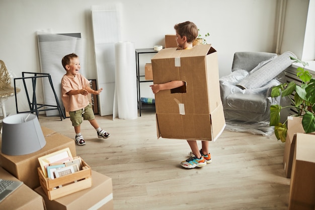 Retrato de cuerpo entero de dos hermanos con cajas de cartón y jugando mientras la familia se muda a la nueva ...