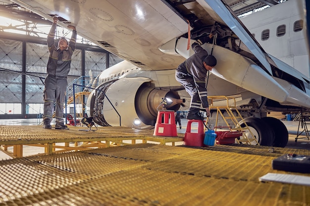 Retrato de cuerpo entero de dos ingenieros en uniforme de fijación y comprobación de aviones comerciales en el hangar