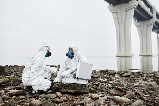 Retrato de cuerpo entero de dos trabajadores con trajes de materiales peligrosos que recogen muestras de sondas por agua tóxica fue ...
